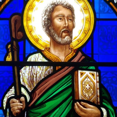 Stained glass window depicting a saint with halo, staff, and Gospel book